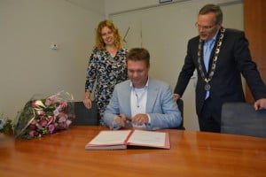 Onder het toeziend oog van burgemeester Luteijn en het andere herbenoemde lid van de RKC, Monique van Amelsvoort, tekent de nieuwe voorzitter, Peter Bakhuizen, het document waarmee zijn officiële benoeming een feit is.