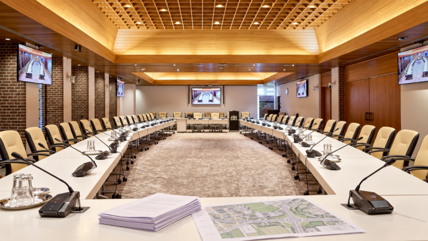 Raadszaal van gemeente Hoeksche Waard met vergaderstukken en een kaart van een ontsluitingsroute.